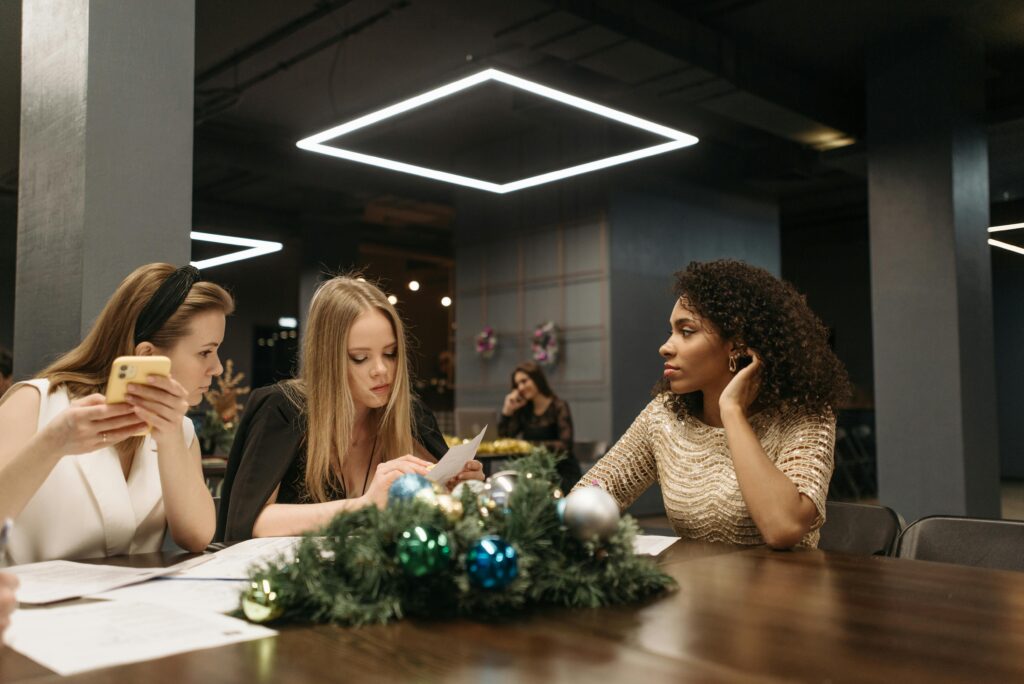 Three women in an office setting celebrating or working during a festive holiday gathering.